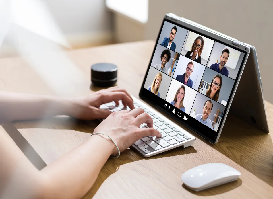 Hände auf der Tastatur – auf dem Bildschirm läuft eine Videokonferenz mit neun Teilnehmenden